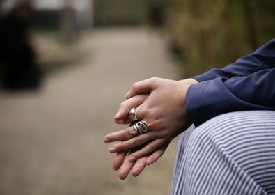 Close-up of a woman's hand showing intricate rings on her fingers, with blurred pathway in the background.