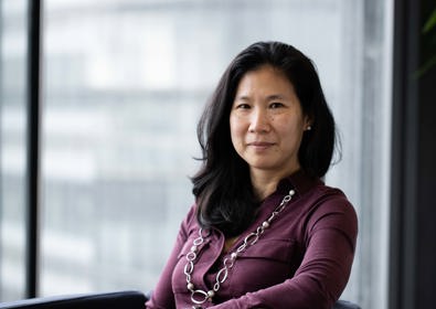 Portrait of a woman wearing a purple dress, sitting indoors with a window background that filters soft natural light.