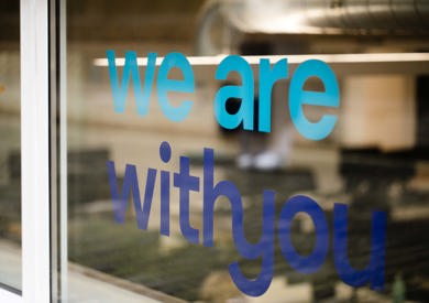 Office door with the words "we are with you" printed on it, visible indoor office setup with monitors.