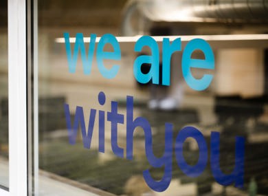 Office door with the words "we are with you" printed on it, visible indoor office setup with monitors.