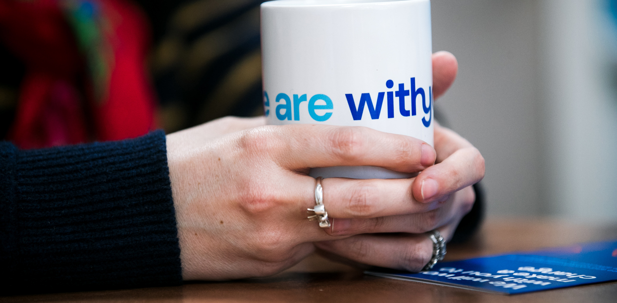 Close-up of a person's hands holding a white mug with the words "Withyou" in blue text.