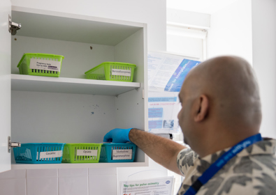 A healthcare worker, seen from behind, reaches for supplies in a labeled hospital storage cabinet.