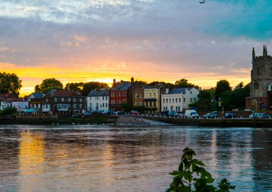 A view over Richmond river, with a silhouette of a grand church and colourful houses lining the waterfront, reflecting in the water.